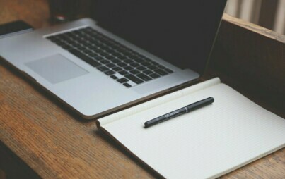 Zdjęcie przedstawiające laptop, notes i długopis leżące na biurku